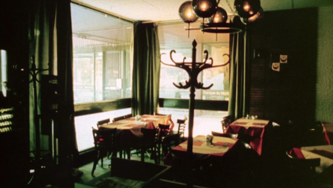 Shivers (1975) movie still: establishing — An empty dining area features rows of tables with red and white linens. A wooden coat rack stands…