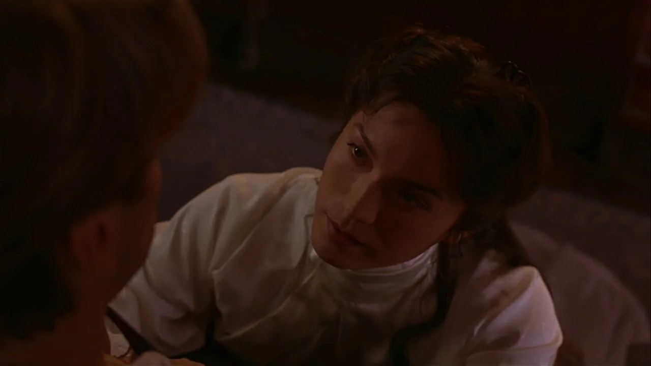 M. Butterfly (1993) movie still: closeup — An interior space with dim, warm lighting obscuring architectural details in darkness. A woman with dark…