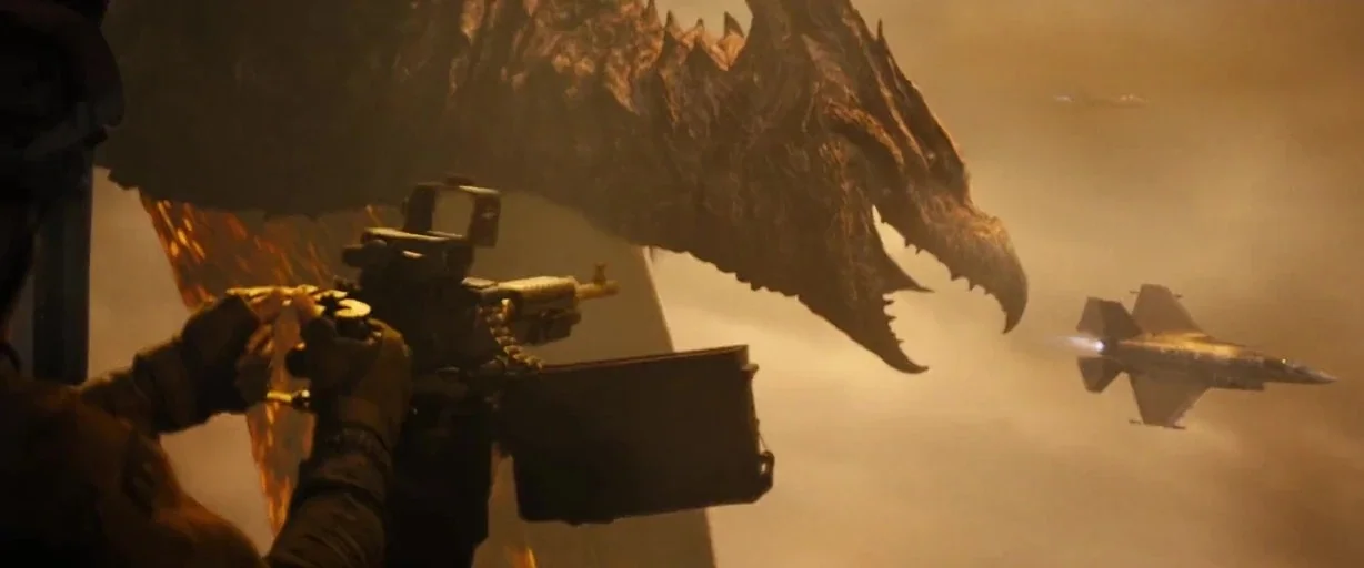 Godzilla: King of the Monsters (2019) movie still: medium — A soldier inside a transport aircraft aims a machine gun at a large dragon. A fighter…