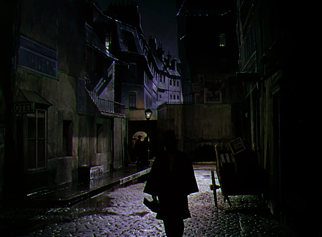 Phantom of the Opera (1943) movie still: fullbody — A narrow European-style cobblestone street at night is framed by multi-story buildings. A…