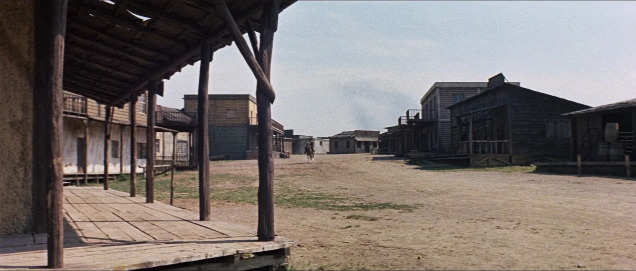 Texas, Adios (1966) movie still: wide — A dusty, unpaved main street stretches through a wooden frontier town in daylight. Weathered storefronts…