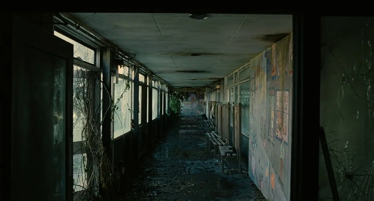 Children Of Men (2006) movie still: establishing — A long, neglected school corridor features rows of windows and peeling paint on murals. Debris…