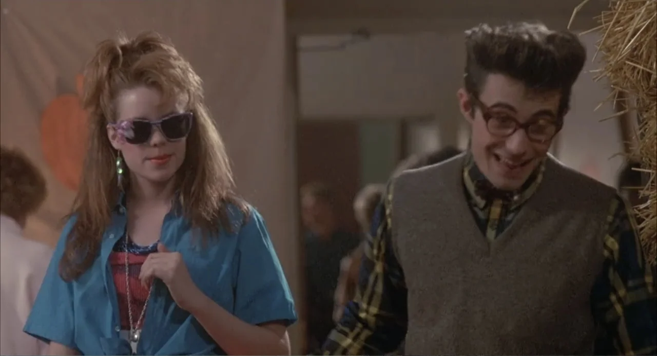 Teen Witch (1989) movie still: medium — A high school gymnasium decorated for an event with hay bales and banners. A girl with sunglasses walks…