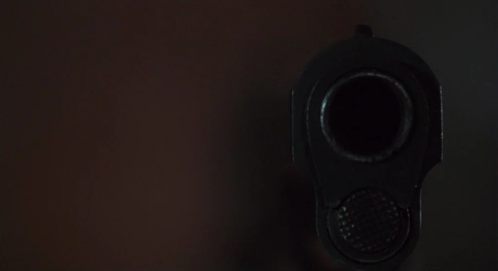 The Crossing Guard (1995) movie still: closeup — A dark, underexposed environment contains only the barrel of a pistol. The weapon is aimed directly…