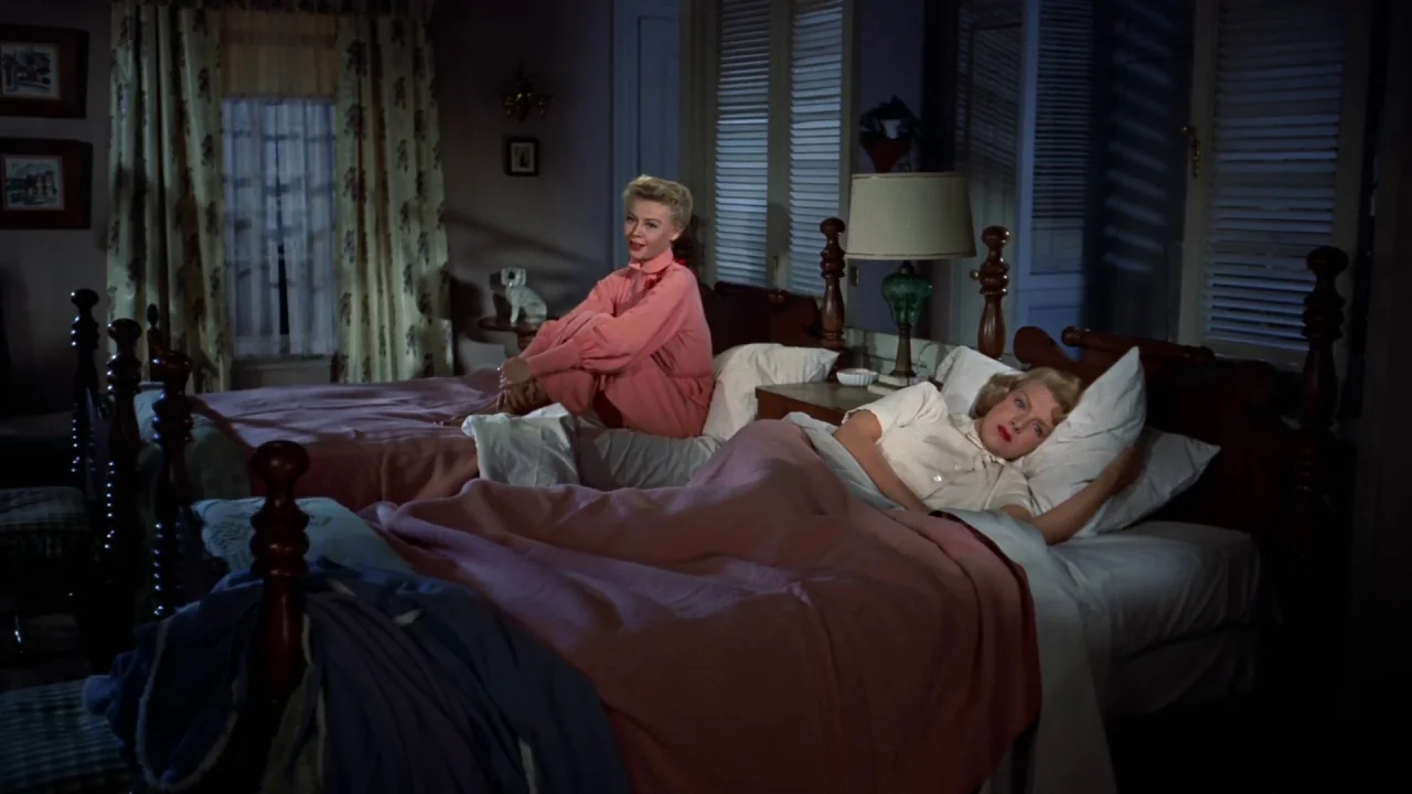 White Christmas (1954) movie still: wide — A 1950s bedroom contains two matching wooden twin beds with patterned curtains. Two blonde women in…