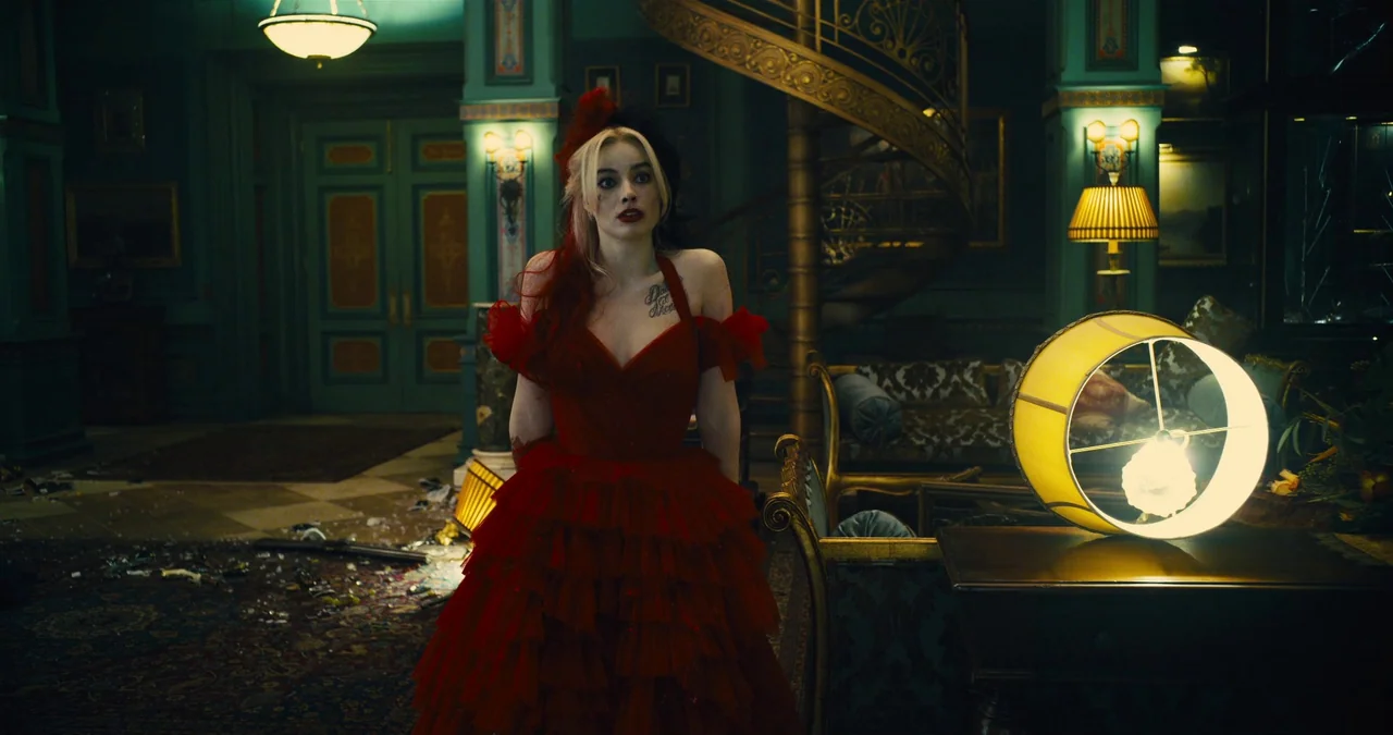 The Suicide Squad (2021) movie still: fullbody — A lavish mansion foyer is dark and filled with debris scattered across the floor. A woman in an…