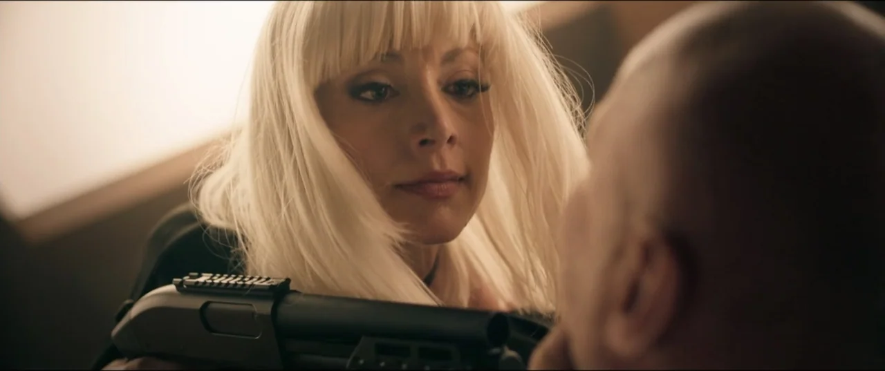 Risqué (2025) movie still: closeup — An interior space provides the backdrop for a tense confrontation between two individuals. A woman with…