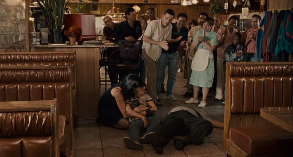 Choke (2008) movie still: wide — A crowded diner interior with brown booths and wood paneling walls. A woman kneels on the tile floor attending to a…