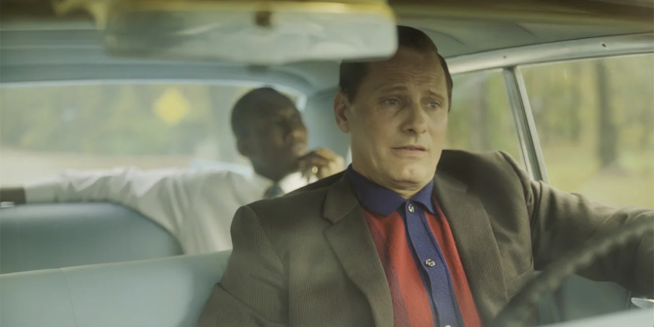 Green Book (2018) movie still: medium — The interior of a vintage sedan features light blue vinyl seats and headrests. A man drives the vehicle…