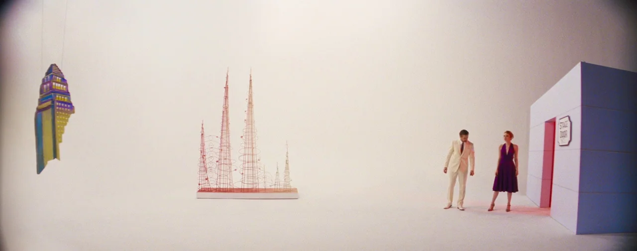 La La Land (2016) movie still: wide — A minimalist studio set features a stark white environment with suspended stylized props. A man in a light…