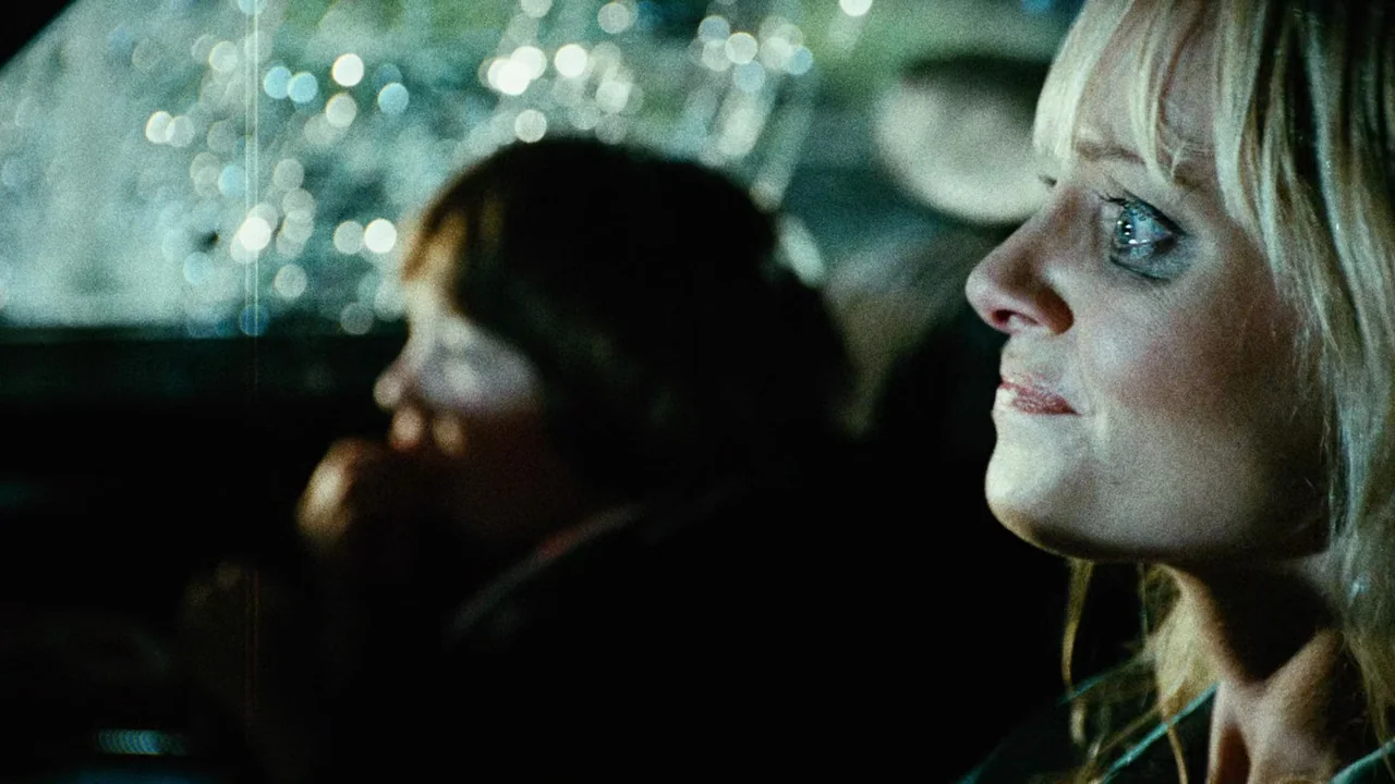 Planet Terror (2007) movie still: closeup — Inside a dark car at night looking out at blurred city lights through glass. A blonde woman in the…