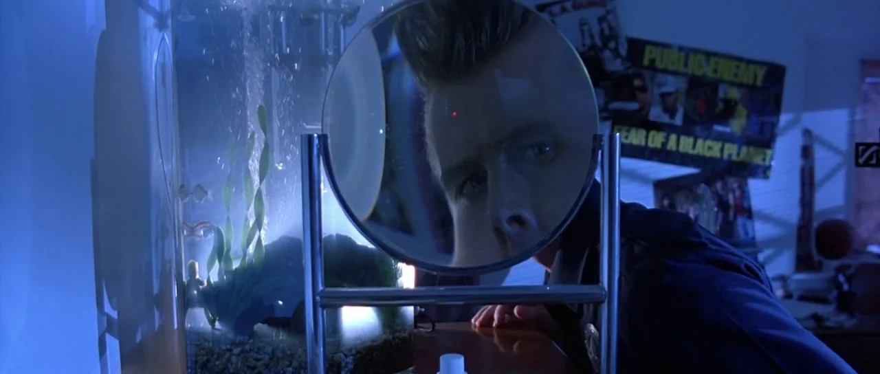 Terminator 2: Judgement Day (1991) movie still: medium — A dimly lit room features a glowing aquarium and a Public Enemy poster on the wall. A man…