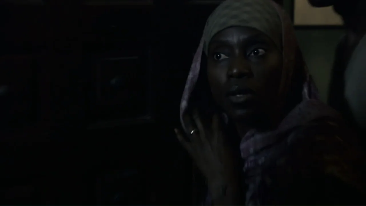 Quarantine (2008) movie still: closeup — A dark indoor space with minimal light falling across the side of a face. A woman wearing a head covering…