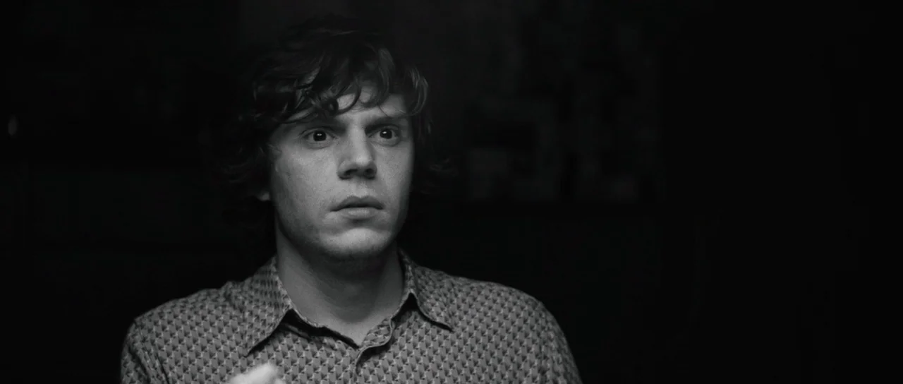 American Animals (2018) movie still: closeup — A man stands against a dark, undifferentiated background in a dimly lit space. He looks slightly…