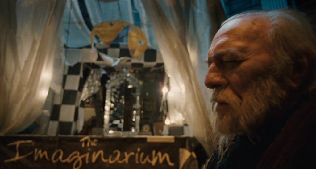 The Imaginarium of Doctor Parnassus (2009) movie still: closeup — A dimly lit, makeshift booth features translucent curtains and a checkerboard…