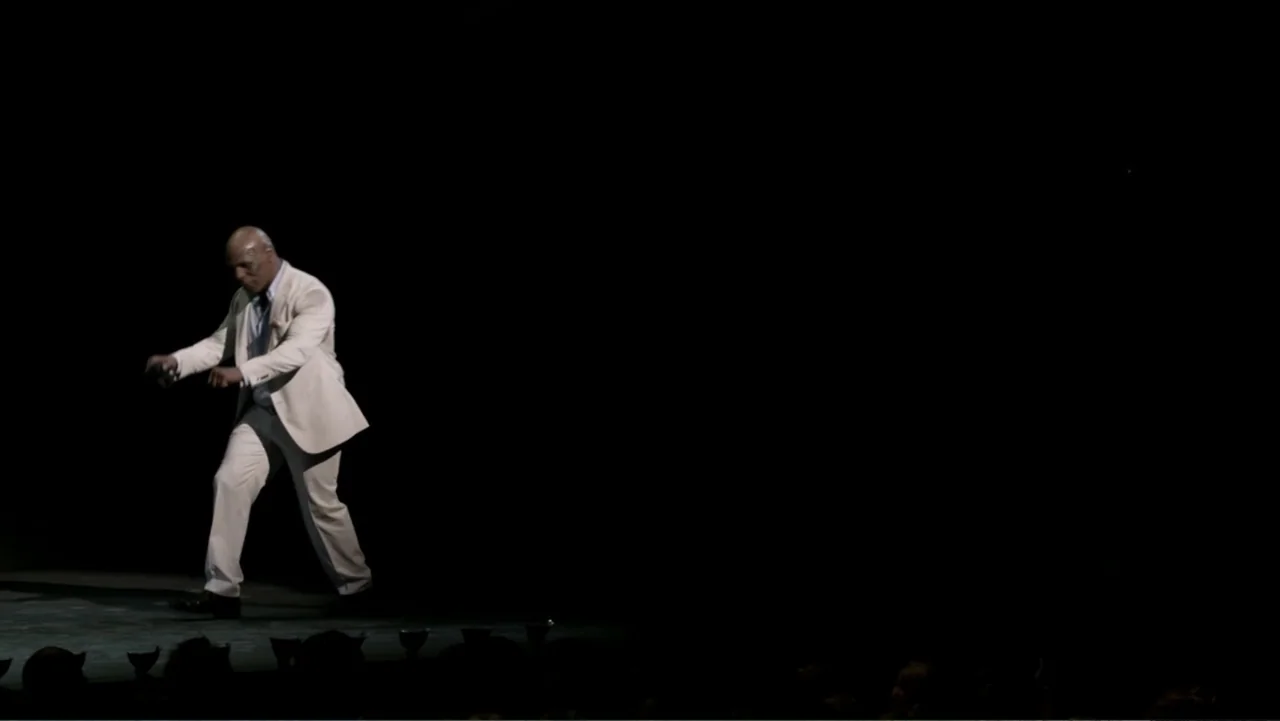 Mike Tyson: Undisputed Truth (2013) movie still: fullbody — A dimly lit stage is cast in total shadow except for one central spotlight. A man in a…