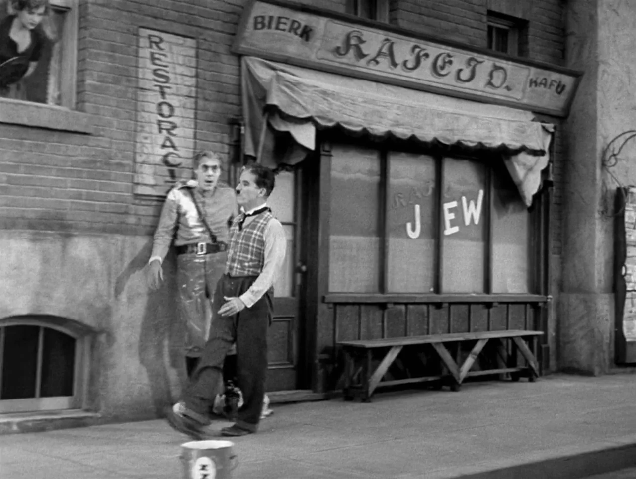 The Great Dictator (1940) movie still: fullbody — A European-style storefront features painted signs with faux-foreign lettering and the word Jew. A…
