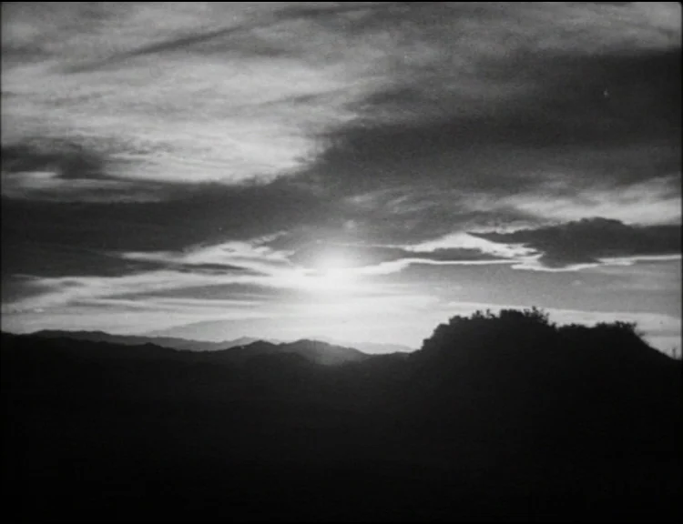 Dracula (1931) movie still: establishing — A dark, hilly landscape sits under a vast, cloud-filled sky at dusk. The setting sun illuminates the…