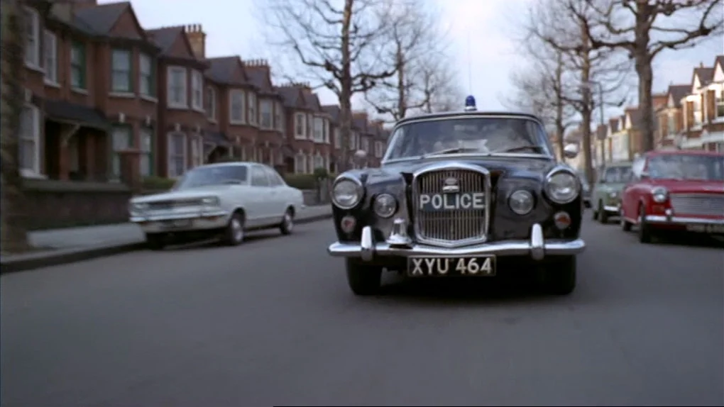 The Sorcerers (1967) movie still: wide — A quiet residential street is lined with rows of identical two-story brick houses. A vintage black police…