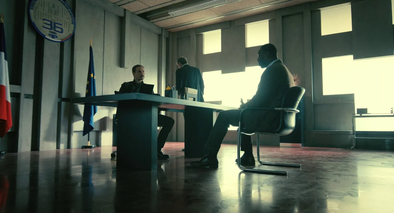 The Killer (2024) (2024) movie still: wide — A modern, sterile office features grey concrete walls and large rectangular windows. Three men occupy…