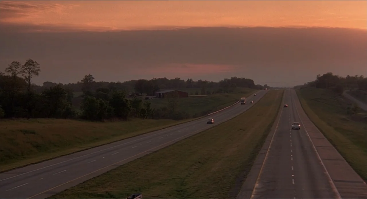 Rain Man (1988) movie still: establishing — A long stretch of highway winds through a flat rural area under a sunset sky. Multiple cars travel along…