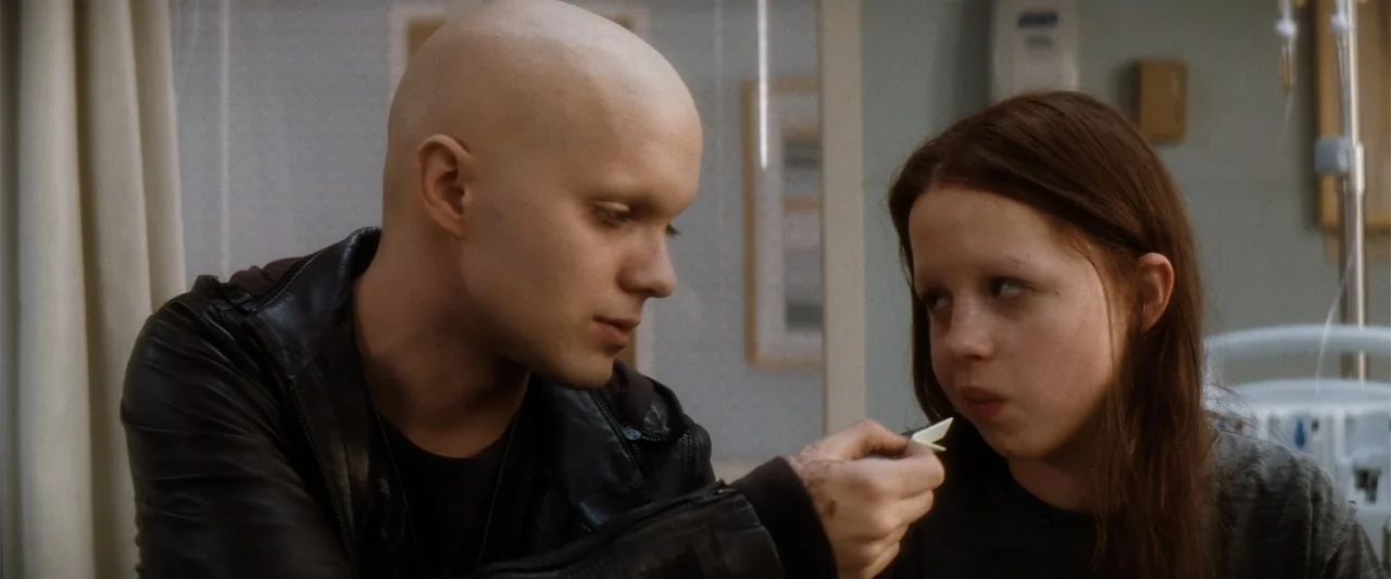 My Sister's Keeper (2023) movie still: medium — A sterile medical room features a curtain and an intravenous drip stand. A bald man leans in while…