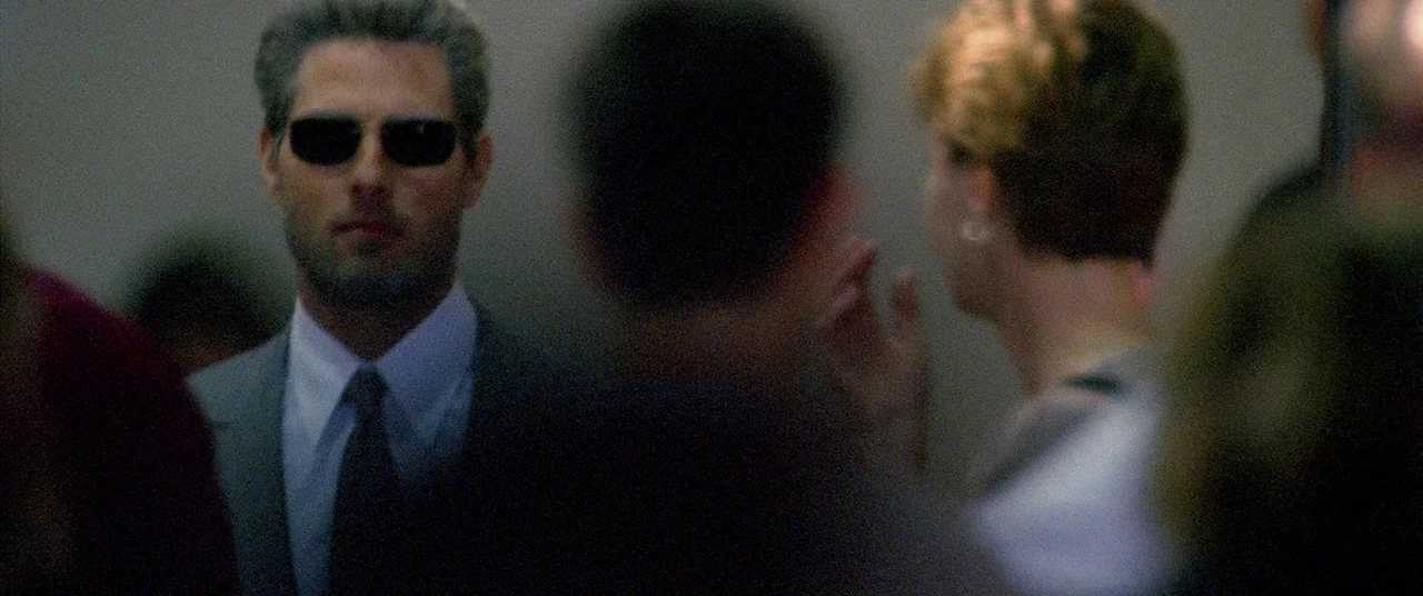 Collateral (2004) movie still: medium — A dimly lit interior of an elevator with metallic grey walls and several occupants. A man in a suit and…