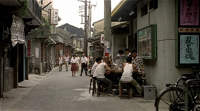 A Time To Love and A Time To Die (1985) movie still: wide — A narrow residential alleyway in East Asia features low-rise buildings and weathered…