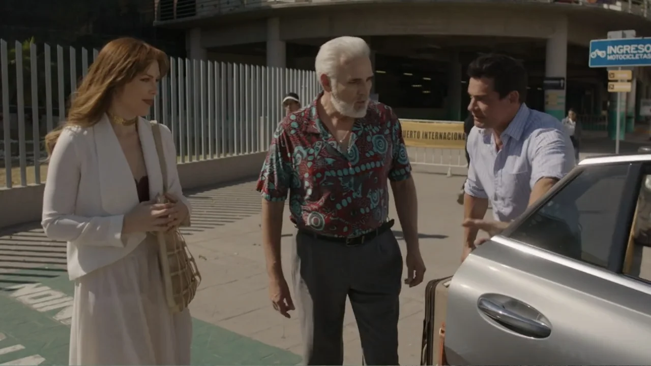 Por Amor al Money (2023) movie still: fullbody — A concrete airport parking lot exterior features a metal fence and directional signage. Three…