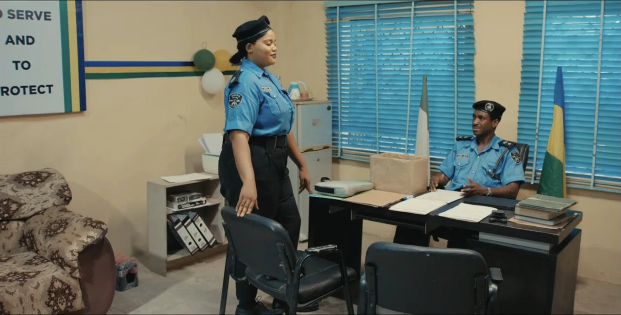 Project Assault (2025) movie still: fullbody — A police station office features light-colored walls, blue window blinds, and official signage. An…