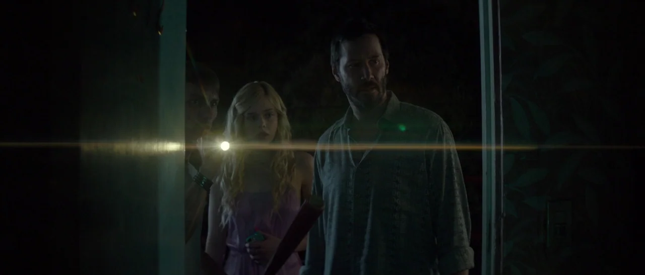 The Neon Demon (2016) movie still: medium — A group stands in a darkened interior doorway at night looking toward the exterior. One man holds a…