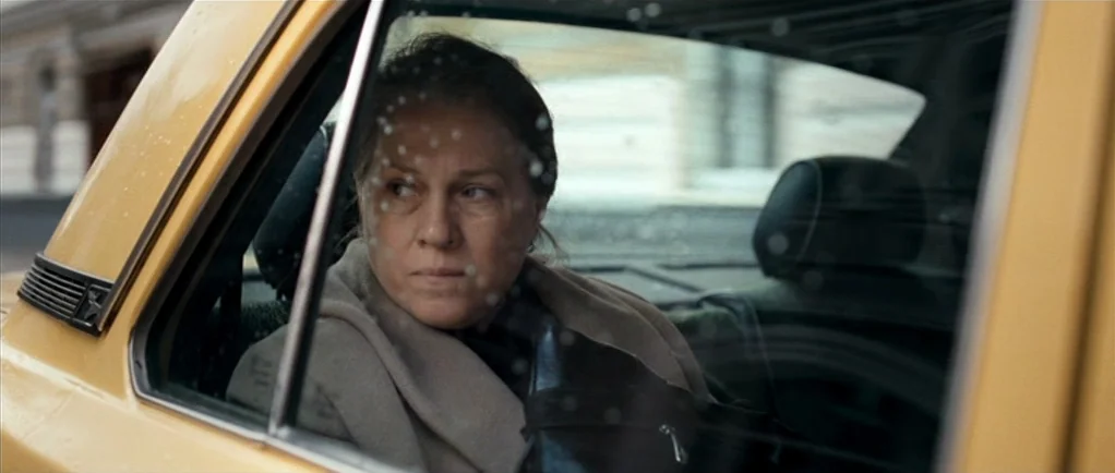 Elena (2011) movie still: medium — The interior of a yellow taxi with rain droplets on the window glass. A woman sits in the backseat and looks…