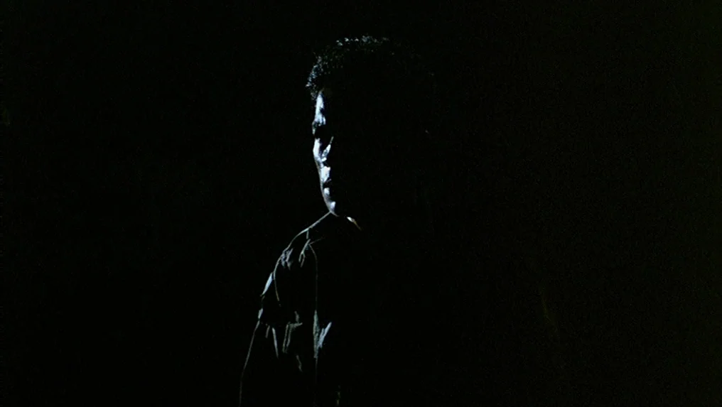 Tropical Malady (2004) movie still: medium — A man stands in an almost completely dark environment with no visible background. The light highlights…