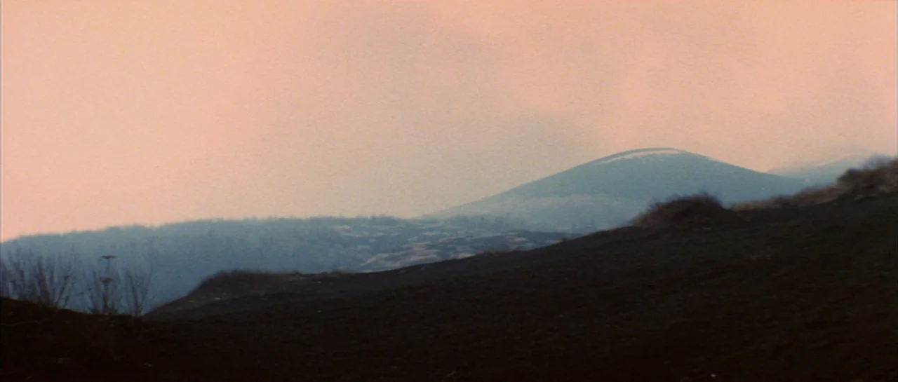 Godzilla Vs Hedorah (1971) movie still: establishing — A vast, barren volcanic landscape stretches toward conical hills under a hazy salmon sky.…