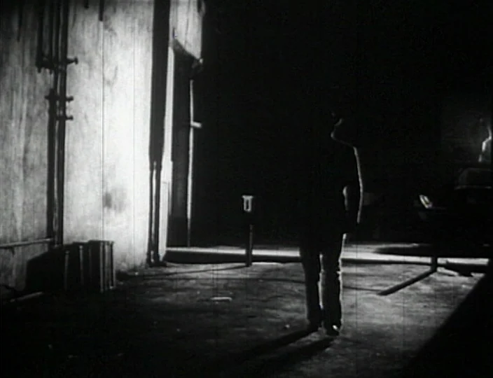 Dementia (Daughter of Horror) (1955) movie still: fullbody — A dark urban outdoor space with vertical pipes mounted on a weathered concrete wall. A…