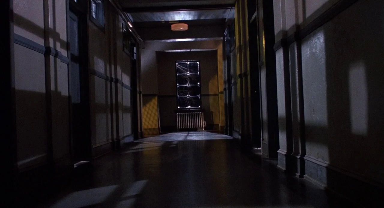 Child’s Play 3 (1991) movie still: establishing — A long corridor with wooden trim and doors leading to rooms on either side. A single window stands…