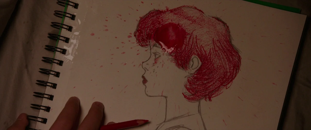 It (2017) movie still: closeup — A notebook rests on a surface with a pencil sketch of a head profile. Red colored pencil and thick red fluid…