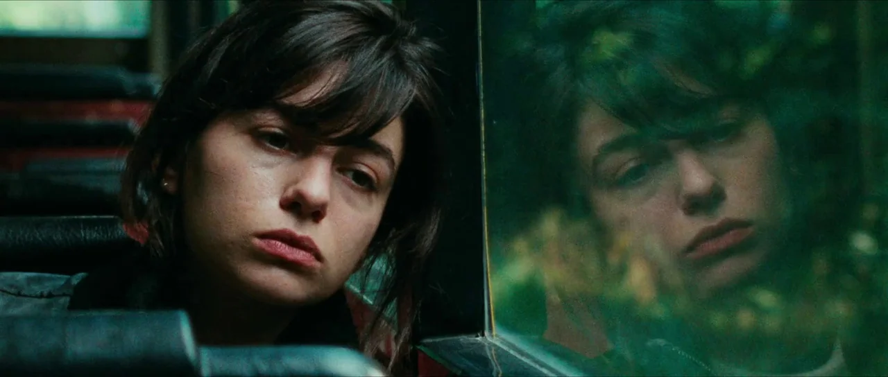 Inexorable (2021) movie still: closeup — A woman sits inside a bus with her head resting near the window. Her reflection is visible in the glass…