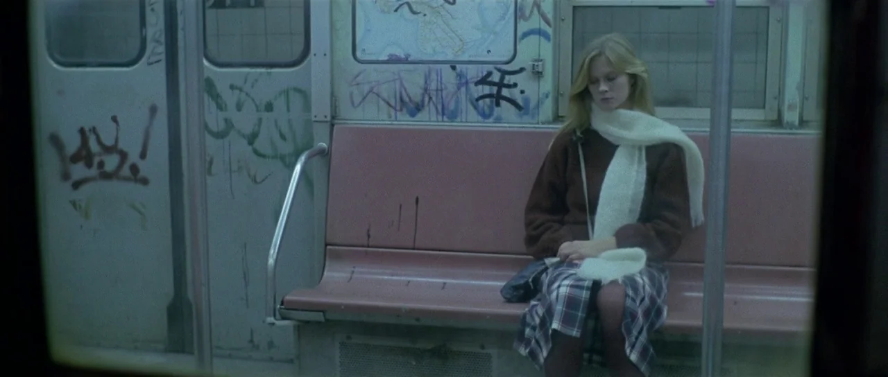 The New York Ripper (1982) movie still: medium — An interior view of a worn 1980s subway car with graffiti-covered walls and plastic seats. A young…