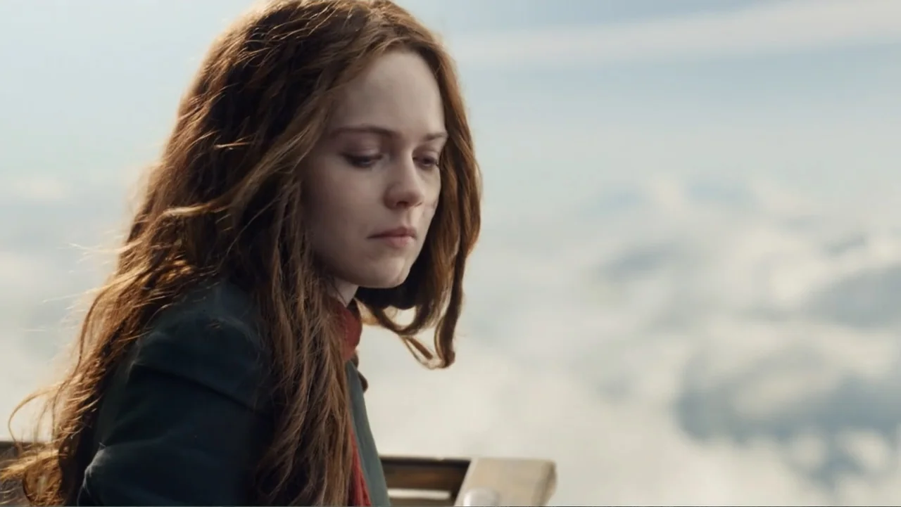 Mortal Engines (2018) movie still: closeup — A woman stands on a high-altitude platform overlooking a vast expanse of clouds. The subject gazes…