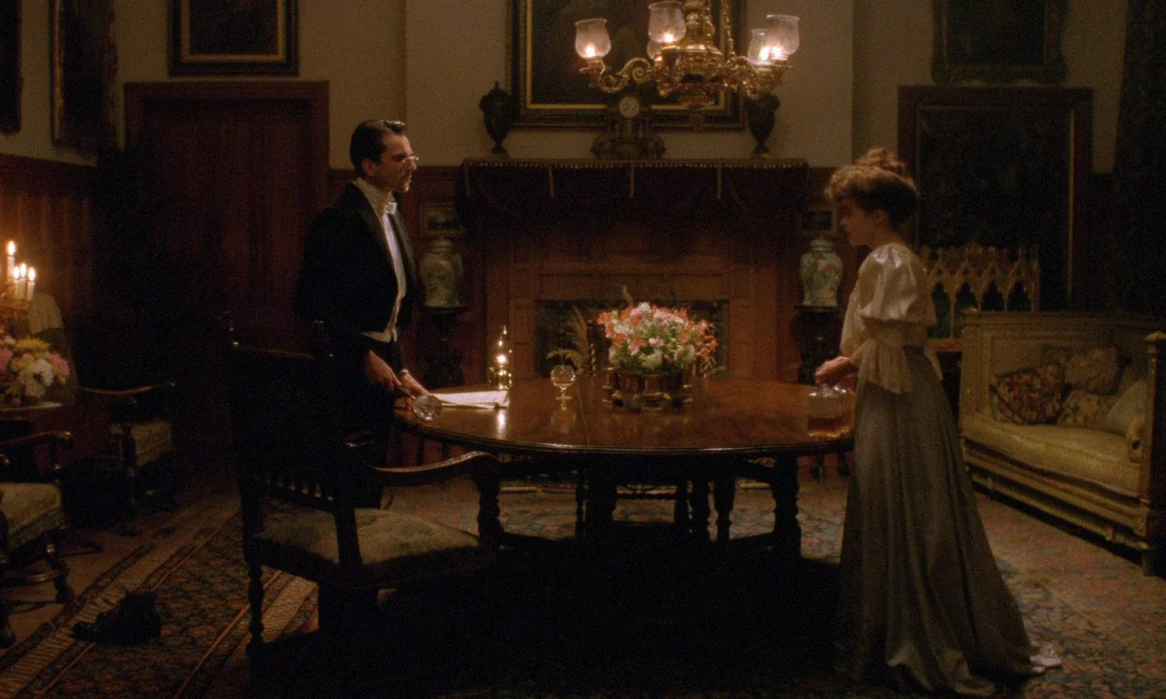 A Room With A View (1985) movie still: wide — An opulent wood-paneled room features a circular table with flowers and a fireplace. A man and a woman…