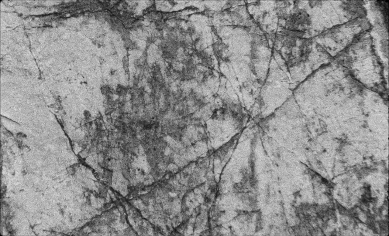 Last and First Men (2020) movie still: closeup — A close-up view of weathered stone featuring intricate cracks and mineral veins. Heavy grain…