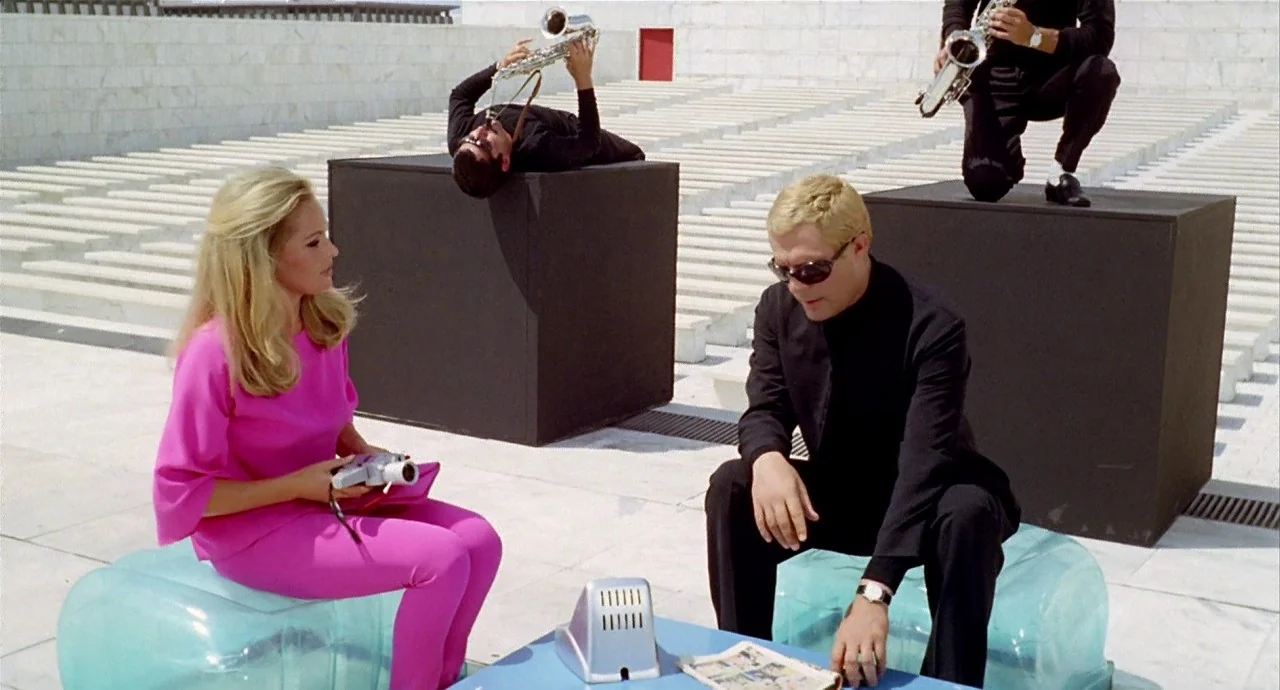 The 10th Victim (1965) movie still: fullbody — A modernist marble stadium with white tiered seating and geometric black sculptural blocks. Two…