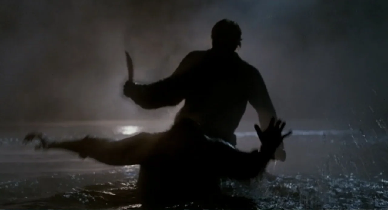 Dangerously Close (1986) movie still: medium — A dark, murky body of water at night with splashing surf in the foreground. Two human silhouettes…