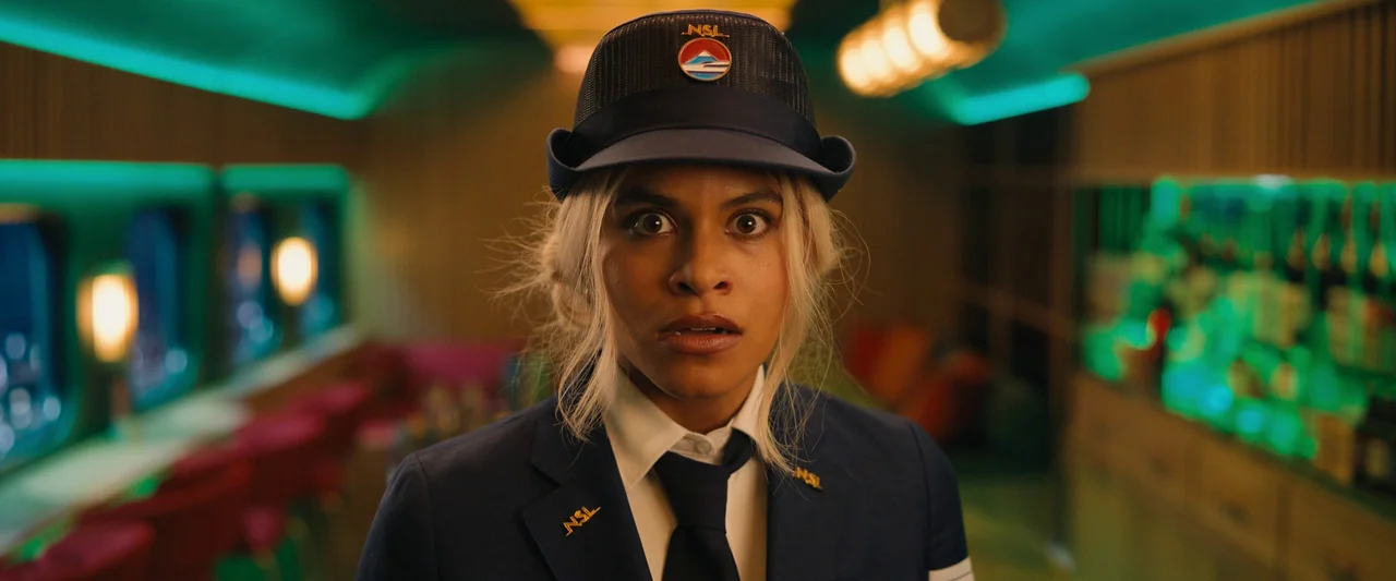 Bullet Train (2022) movie still: medium — The interior of a modern transit vehicle features neon-lit wall panels and warm lamps. A young woman in a…