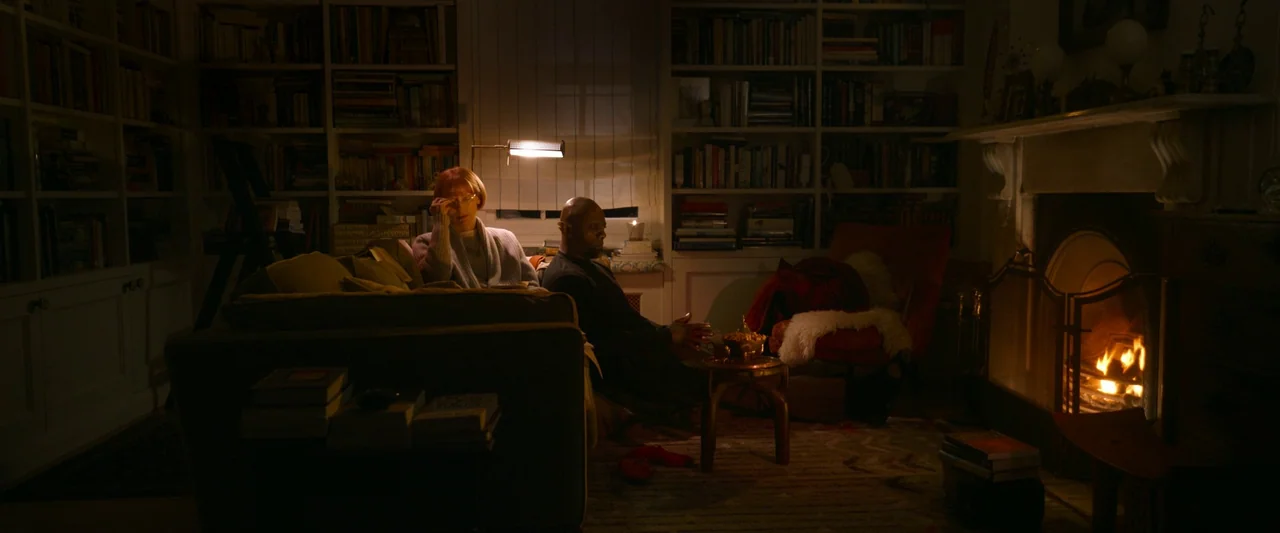 Three Thousand Years of Longing (2022) movie still: wide — A dark home library features floor-to-ceiling bookshelves and a crackling fireplace on…