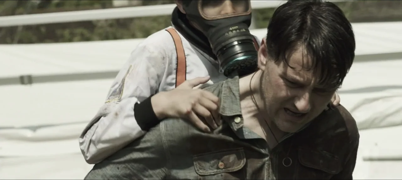 Containment (2015) movie still: medium — A sunny outdoor location with white tent-like structures visible in the blurred background. A child wearing…