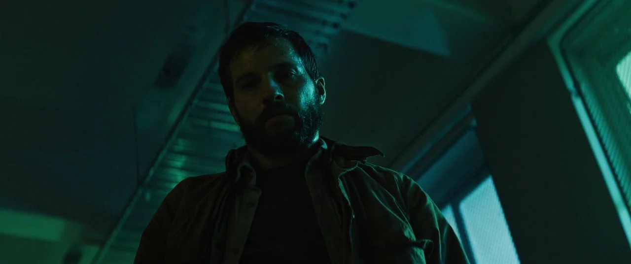 Upgrade (2018) movie still: medium — An industrial hallway with metal wall panels and stairs in the background. A man stands in the foreground…