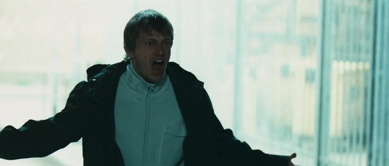Green Street (2005) movie still: medium — A man stands in a bright, sterile stairwell with metal railings and white walls. He shouts loudly while…
