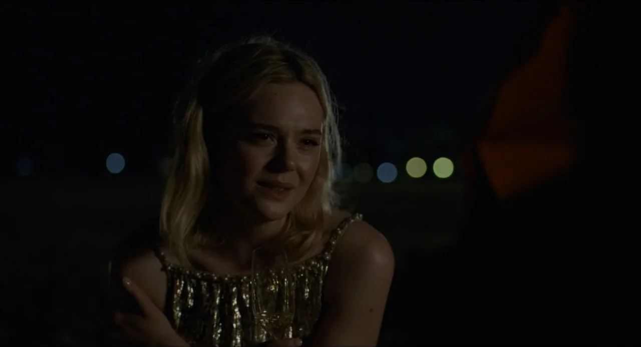 Sentimental Value (2025) movie still: medium — A dark night setting at a beach with distant blurred city lights visible behind the subject. A young…